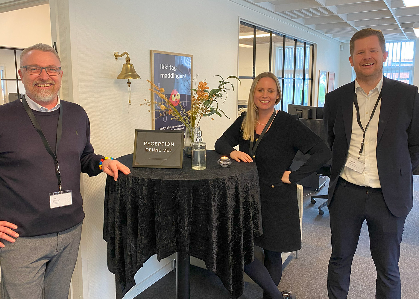Tre Azend-medarbejdere smilende ved et bord, klar til at byde velkommen til et networking-arrangement.