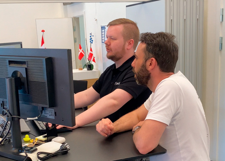 To mænd kigger på en computerskærm mens de diskuterer et projekt på kontoret.